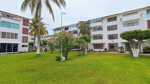 A multi-story hotel with balconies, a well-maintained lawn, and palm trees. - Apartment with pool near the beach in PV (Puerto Vallarta)