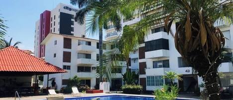 Una piscina con sillas de descanso, palmeras y un edificio con balcones.