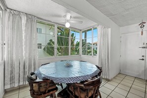 A dining area with a round table, chairs, a ceiling fan, and large windows with curtains. - Apartment with pool near the beach in PV (Puerto Vallarta)