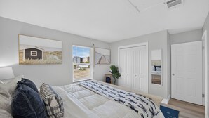 Een slaapkamer met een bed, een raam, een deur en een ingelijste foto aan de muur.