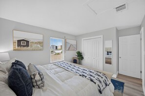Ein Schlafzimmer mit Bett, Fenster, Tür und einem gerahmten Bild an der Wand.