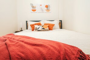 Ein ordentlich bezogenes Bett mit roter Decke, weißen Kissen und einem hölzernen Kopfteil.