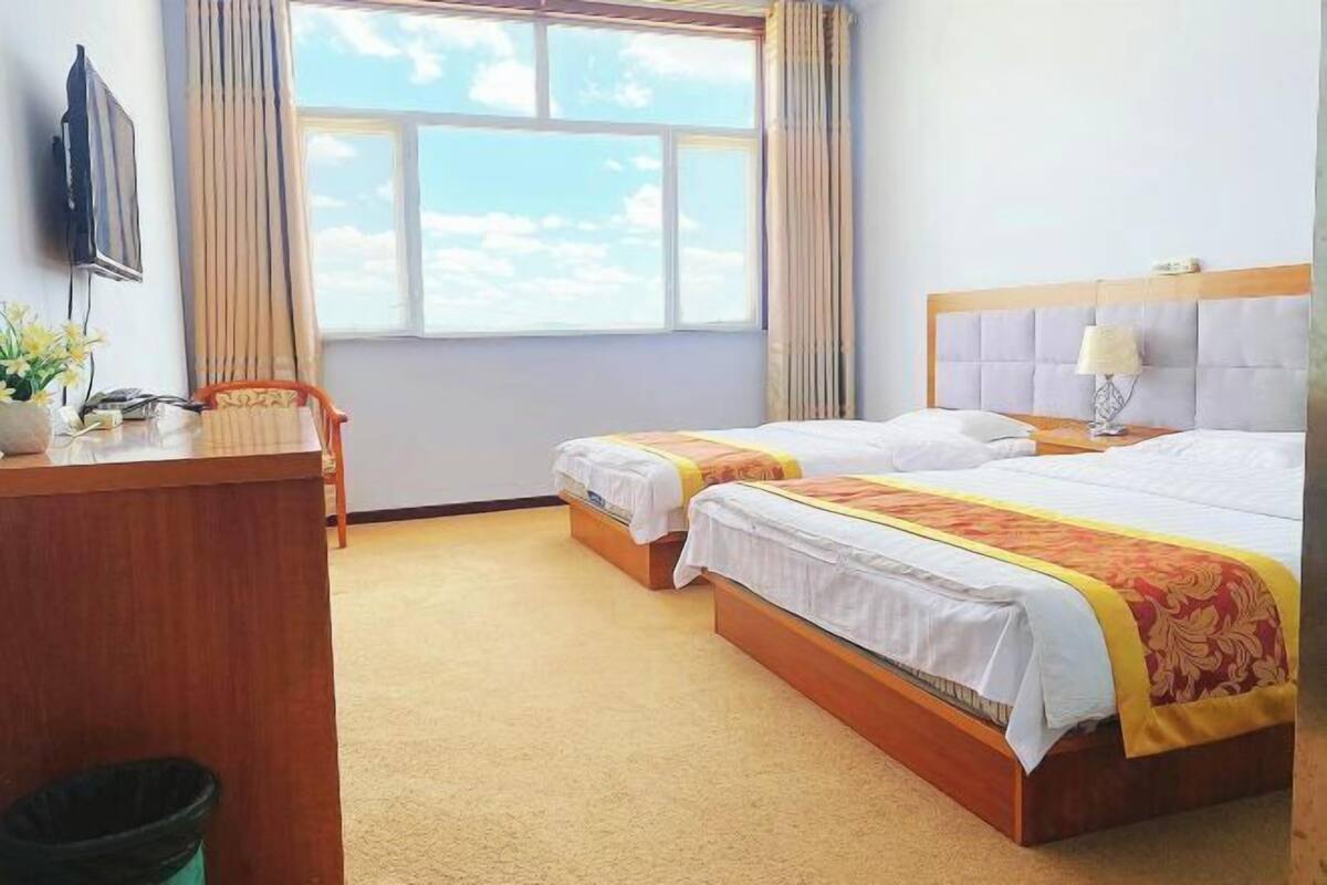 Hotellihuone, jossa on kaksi sänkyä, työpöytä, televisio ja ikkuna, jossa on verhot.
