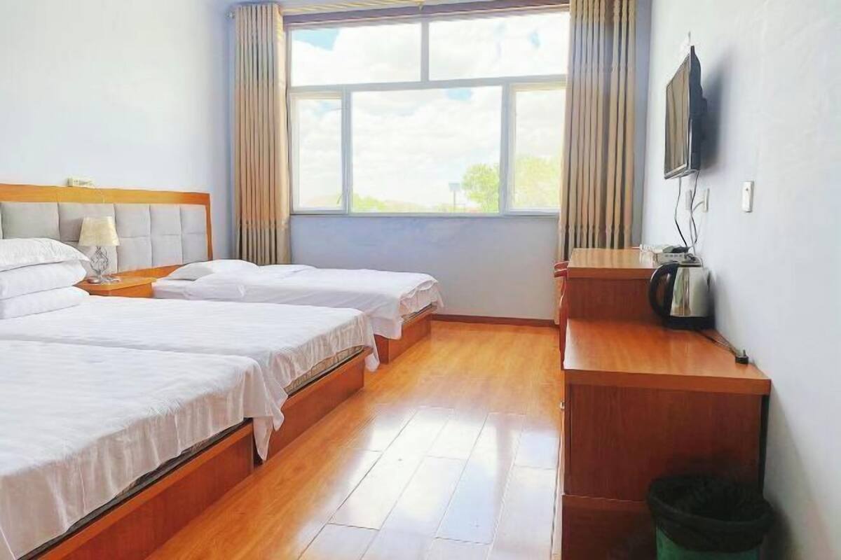Hotellihuone, jossa on kaksi sänkyä, puulattia, televisio ja ikkuna, jossa on verhot.