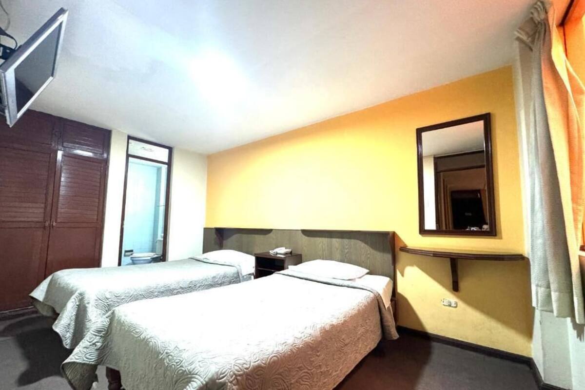 Habitación de hotel con dos camas, un espejo, una mesita de noche y una ventana.