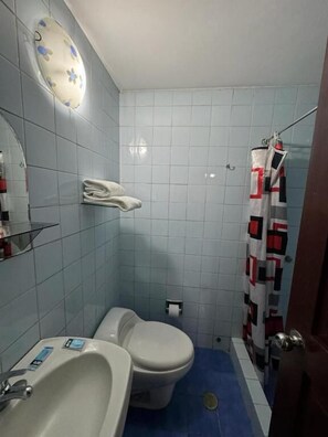 A bathroom with a toilet, sink, and shower curtain. - Hotel Los Angeles (Arequipa)