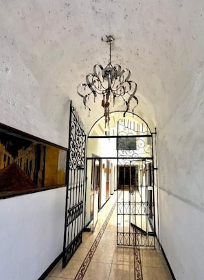 A narrow hallway with a chandelier, a gate, and a mural on the wall. - Hotel Los Angeles (Arequipa)