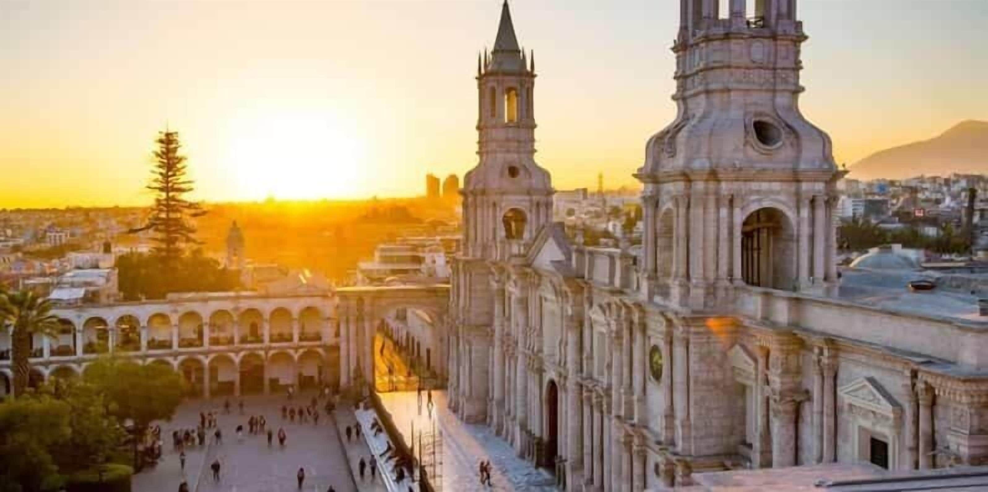 A historic cathedral with a large central nave, two bell towers, and a courtyard with people.
