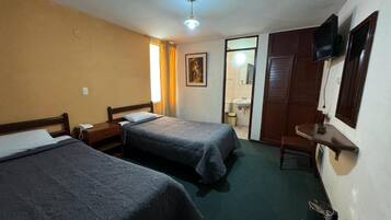 A hotel room with two beds, a television, a desk, and a bathroom visible through an open door.