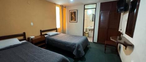 A hotel room with two beds, a television, a desk, and a bathroom visible through an open door.