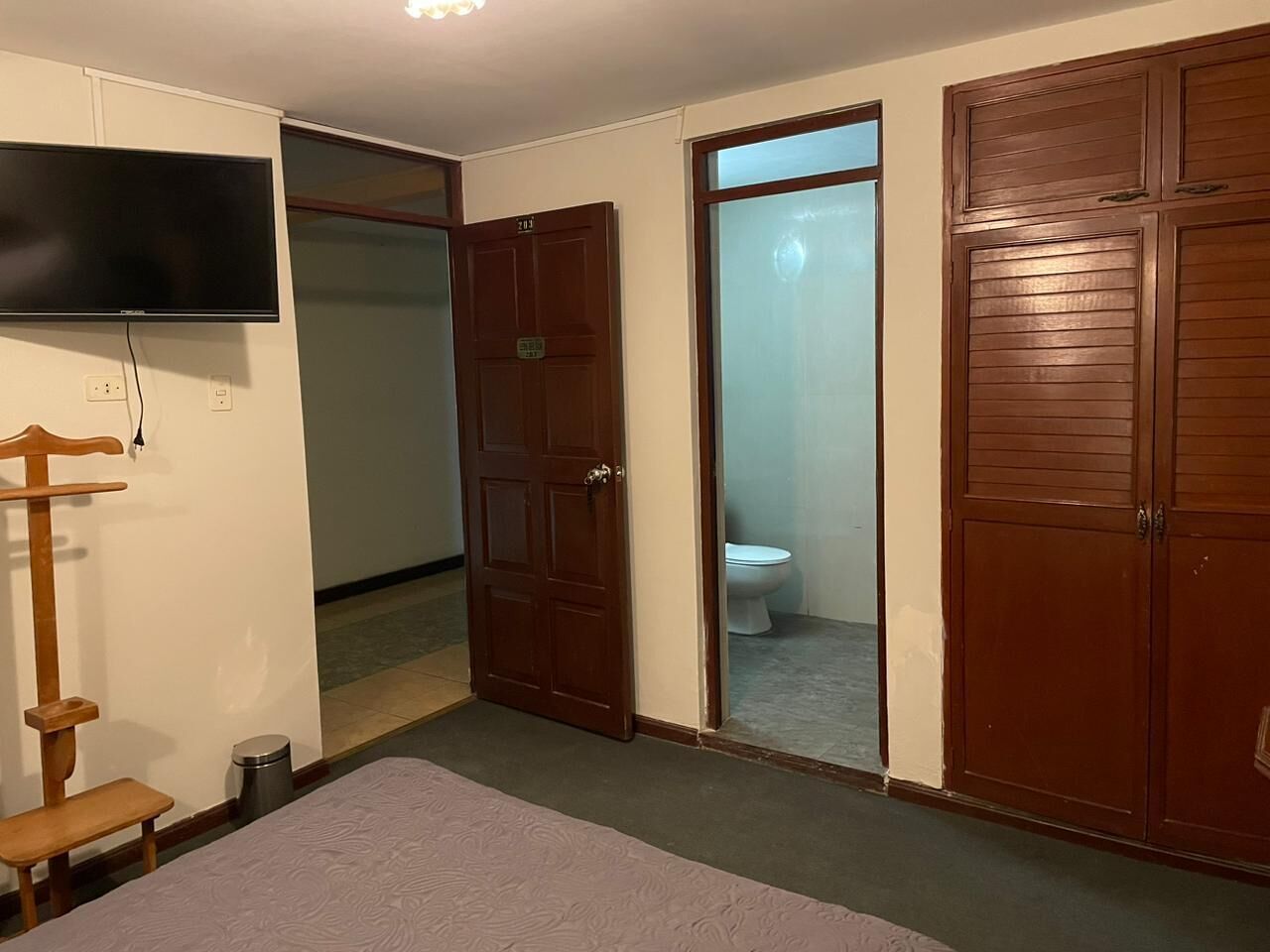 A room with a bed, a wooden bench, a television, and a wardrobe.