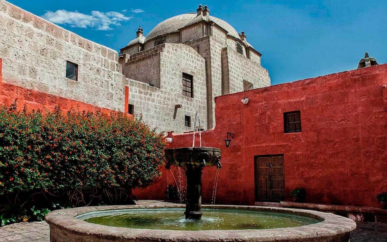 Un patio con una fuente, un edificio con cúpula y un muro rojo.
