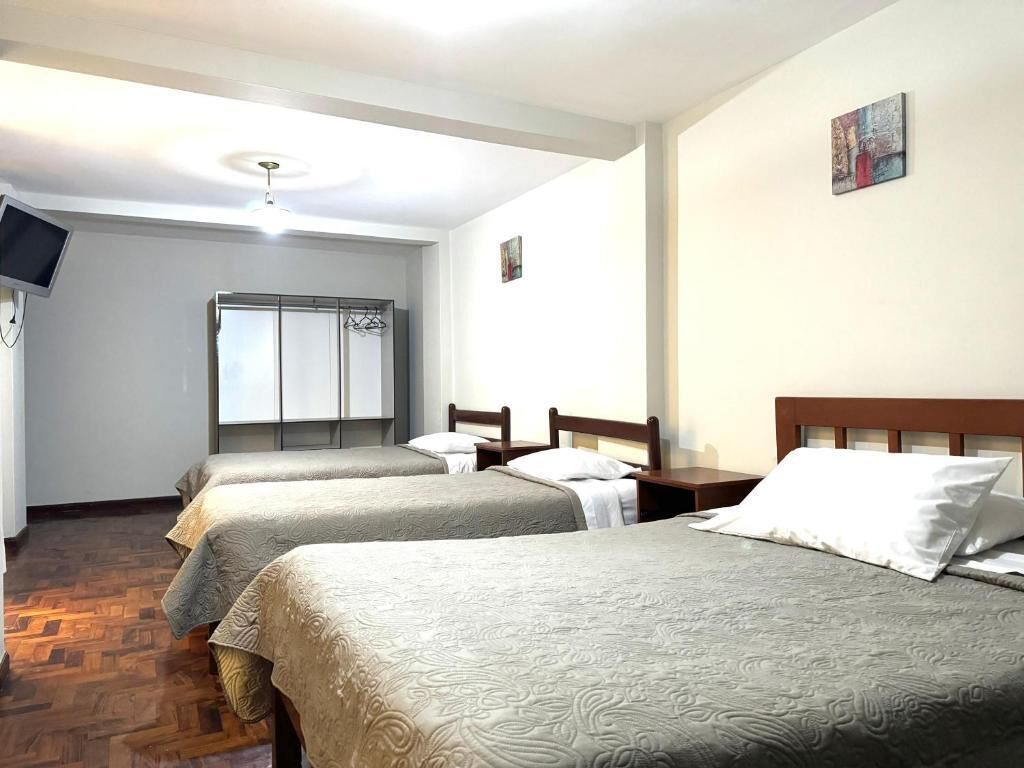 Hotellihuone, jossa on kolme sänkyä, vaatekaappi, televisio ja taulu seinällä.
