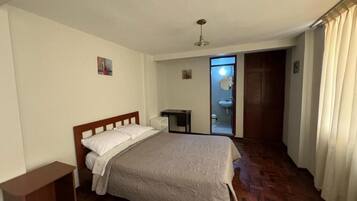 A bedroom with a bed, a bedside table, a wardrobe, and a bathroom visible through an open door.