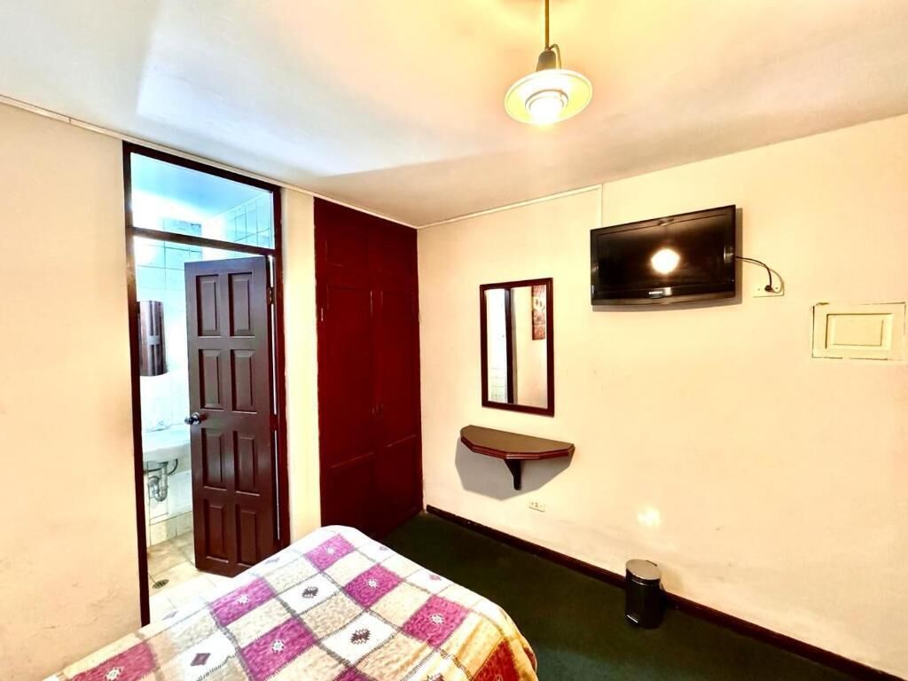 Una habitación con cama, espejo, televisión y puerta que da a un baño.