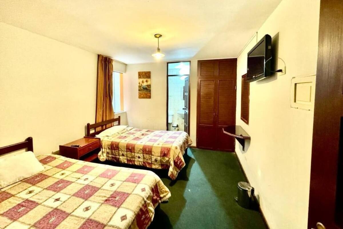 Habitación de hotel con dos camas, televisión, una mesita y una puerta que da a un baño.