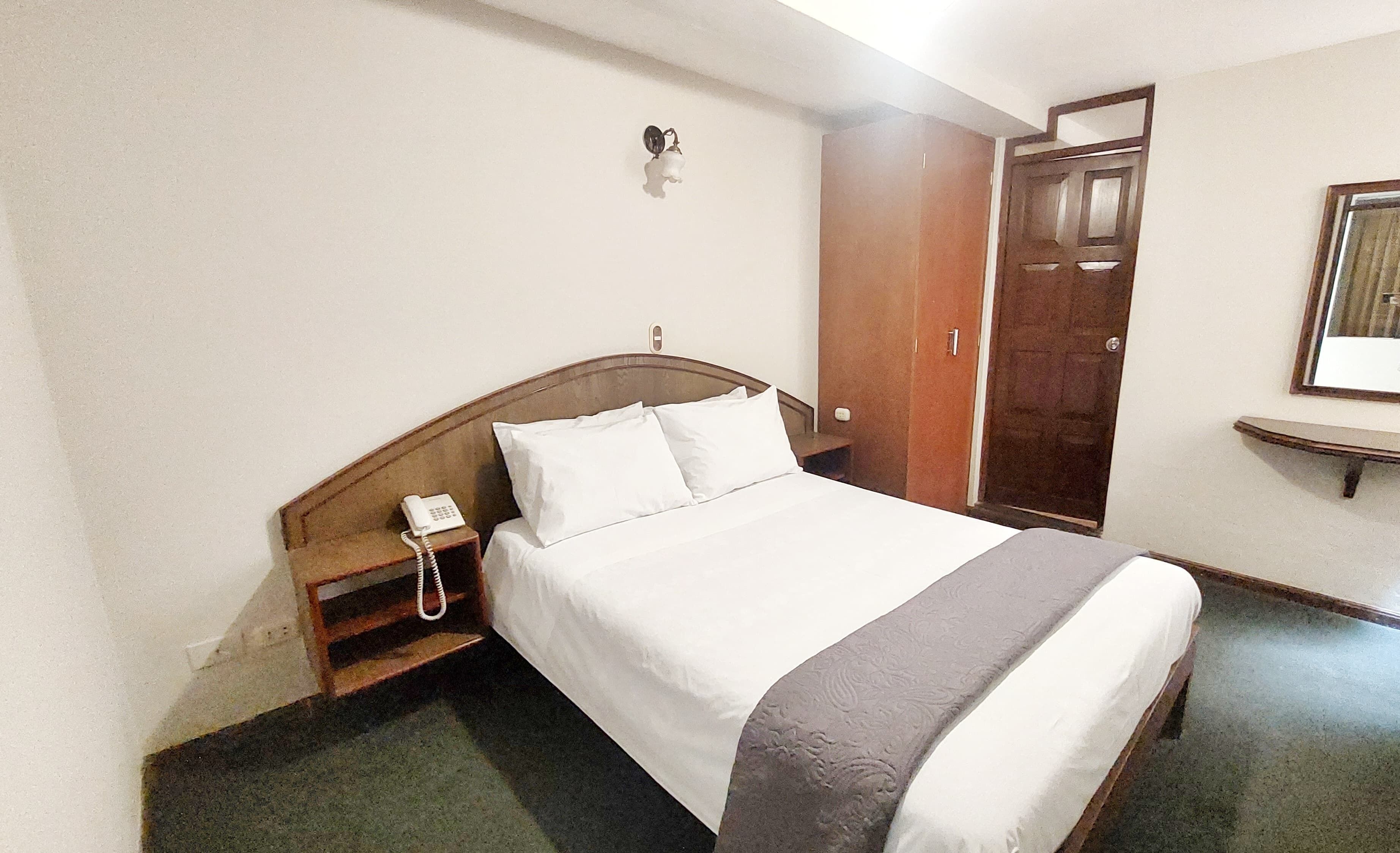 Quarto de hotel com cama, telefone de apoio, guarda-roupa e espelho na parede.