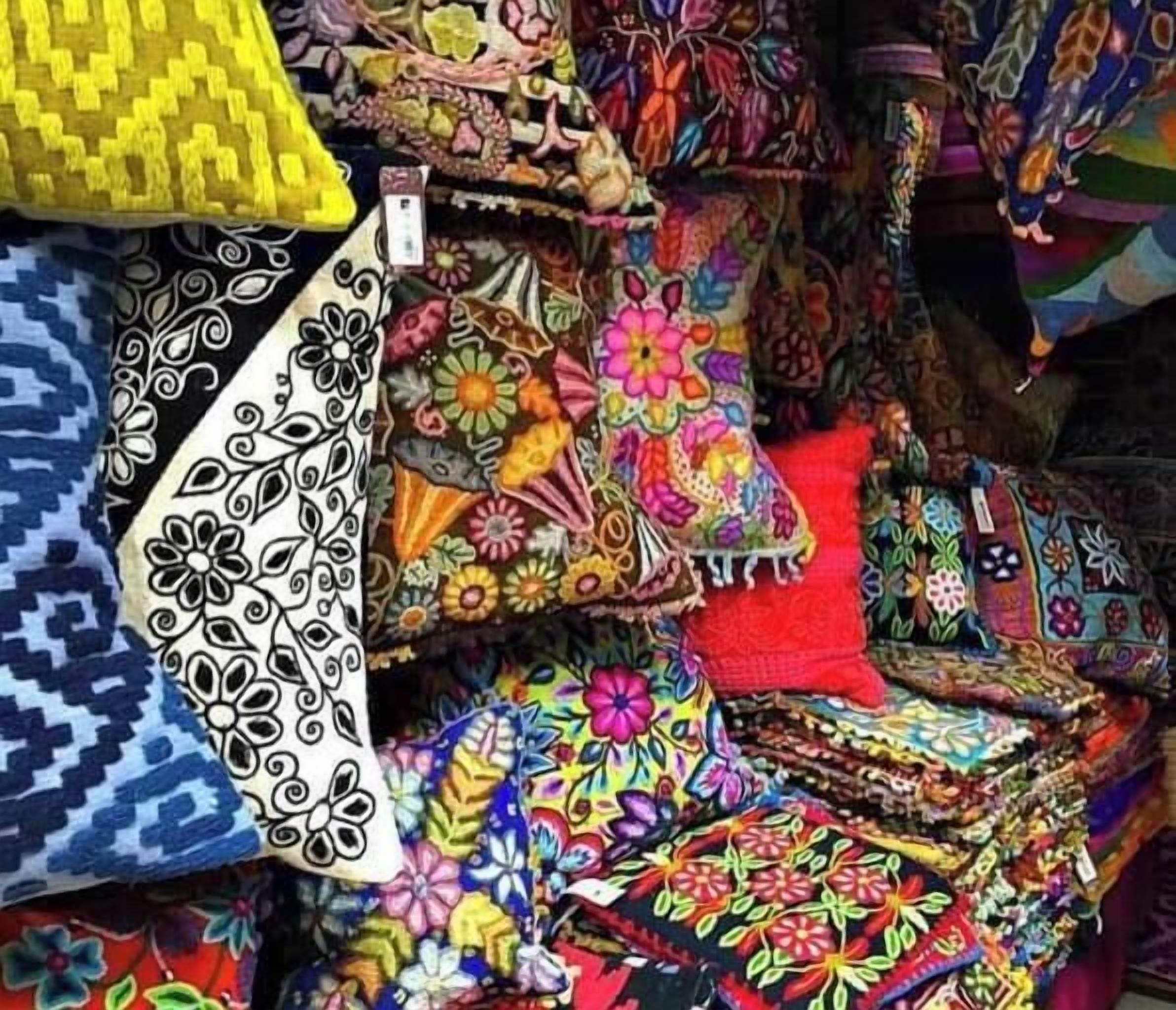 A variety of colorful textiles, including pillows and blankets, displayed in a market setting.