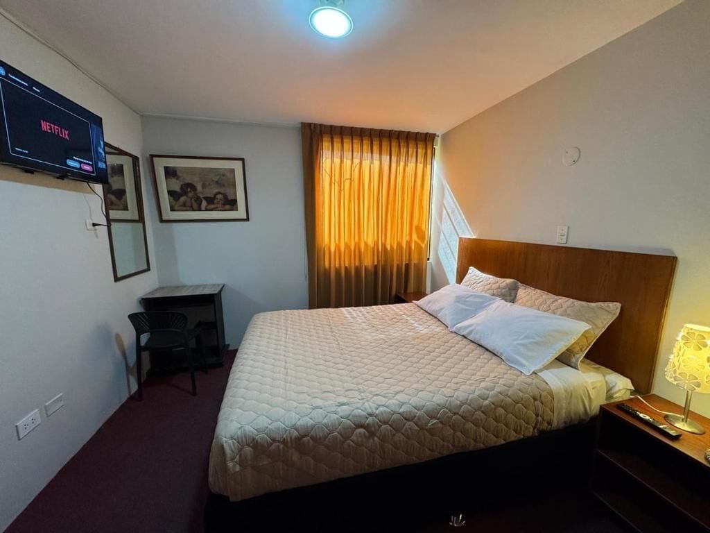 A hotel room with a bed, a desk, a TV, and a window with curtains.