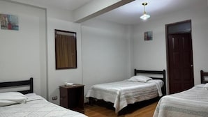 Una habitación con dos camas individuales, piso de madera, un escritorio pequeño y una puerta.