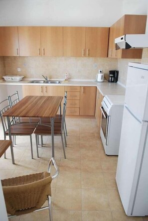 Uma cozinha com armários de madeira, uma pia de aço inoxidável, uma geladeira branca e uma mesa de jantar com cadeiras.