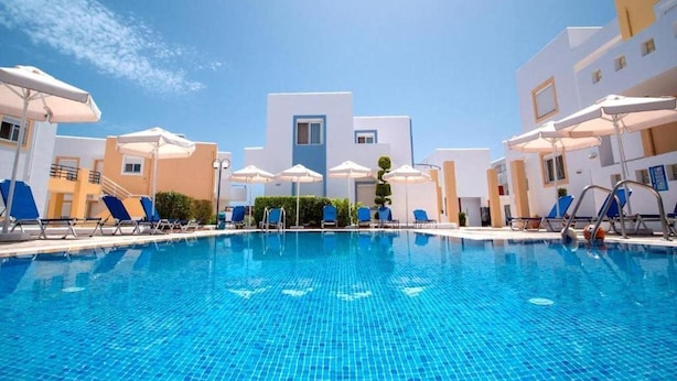 Una piscina con sillas de descanso y sombrillas, rodeada de edificios de estilo arquitectónico moderno.