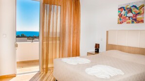 Ein Hotelzimmer mit Bett, Nachttisch, einem Gemälde und Meerblick.