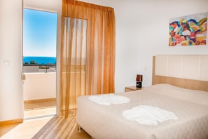 Een hotelkamer met een bed, nachtkastje, schilderij en uitzicht op zee.