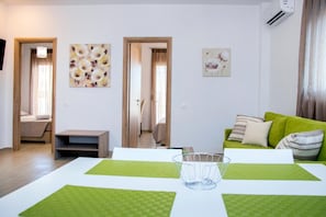 Een moderne woonkamer met een groene bank, een witte salontafel en kunstwerken aan de wanden.
