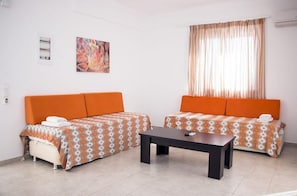 Une piĂšce avec deux canapĂ©s orange, une petite table et une fenĂȘtre avec des rideaux.