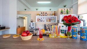 Zona de bar con estantes de botellas de licor, una cesta de fruta, una bebida y latas de Pringles.