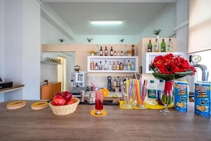 Zona de bar con estantes de botellas de licor, una cesta de fruta, una bebida y latas de Pringles.