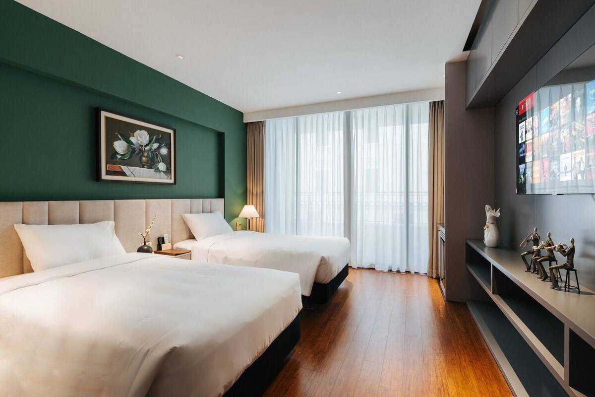 Een hotelkamer met twee bedden, een schilderij, een televisie en een groot raam met gordijnen.