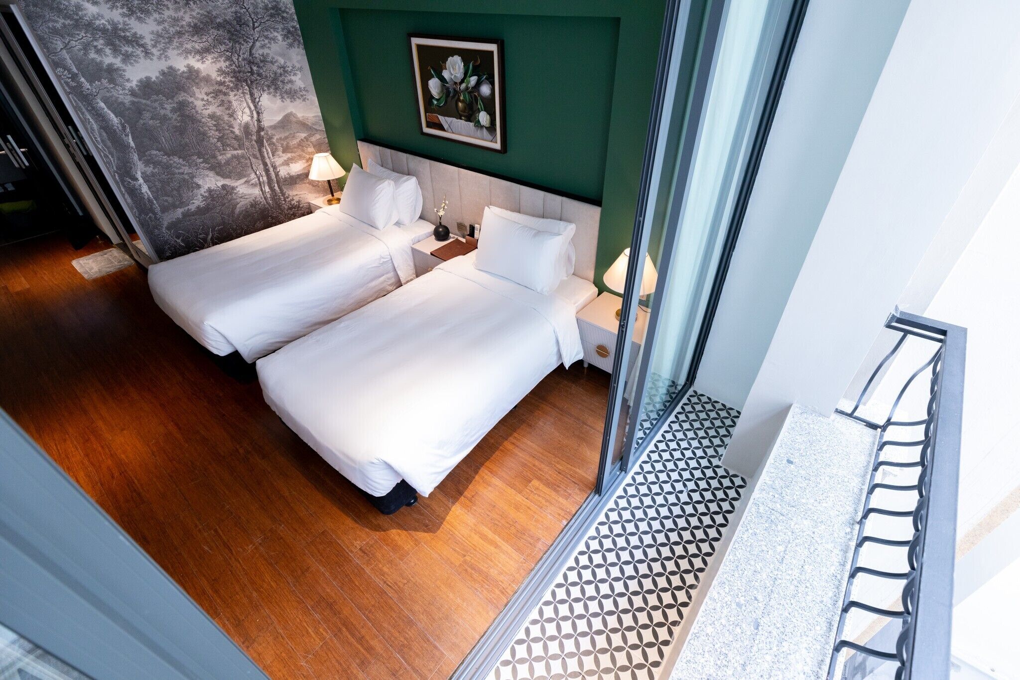 A hotel room with two beds, a large window, a green wall, and a mural.