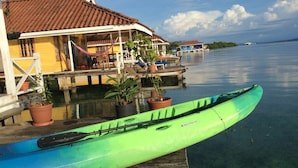 A green kayak on a wooden dock, a yellow building with a red roof, and a calm body of water.