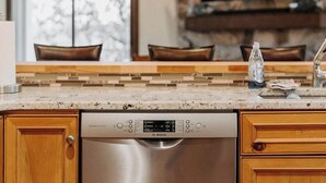 A kitchen with a Bosch dishwasher, wooden cabinets, a marble countertop, and a stone fireplace.