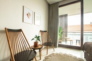 A modern room with two wooden chairs, a small table with a potted plant, a large window with curtains, and a view of a balcony with outdoor furniture.