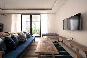 A living room with a sofa, a wooden table, a bench, and a TV mounted on the wall.