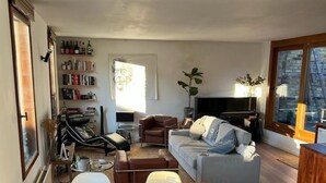Uma sala de estar com sofá, televisão, estante de livros e área de jantar com mesa e cadeiras.