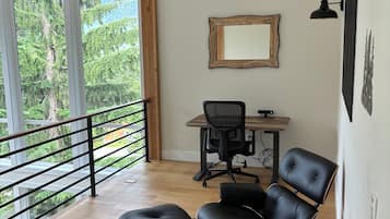 Um interior moderno com teto de madeira, uma escrivaninha com cadeira, uma janela grande com vista para árvores e um abajur preto.