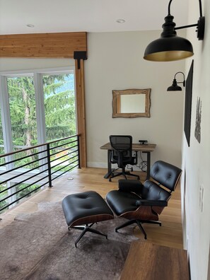 Un intérieur moderne avec un plafond en bois, un bureau avec une chaise, une grande fenêtre donnant sur des arbres et un lampadaire noir.