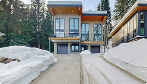 Uma casa moderna de dois andares com garagem, rodeada por neve e árvores.