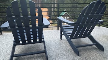 Two Adirondack chairs on a gravel surface with a view of a cabin and forest in the background.