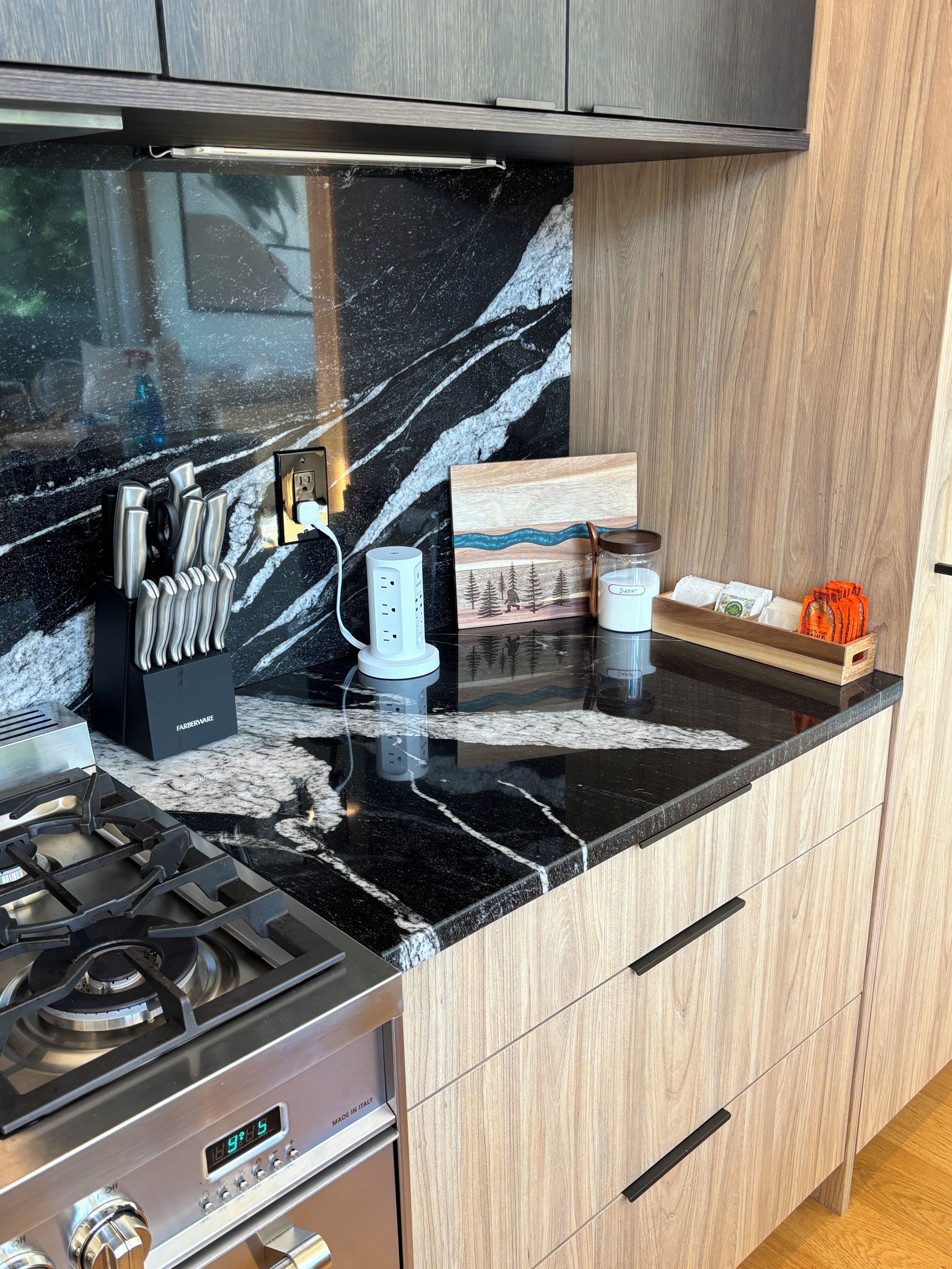 A kitchen with a black marble countertop, a gas stove, a coffee maker, and a knife block.