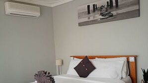 Ein ordentlich bezogenes Bett mit einem hölzernen Kopfteil, einem Deckenventilator und einer Wandklimaanlage.