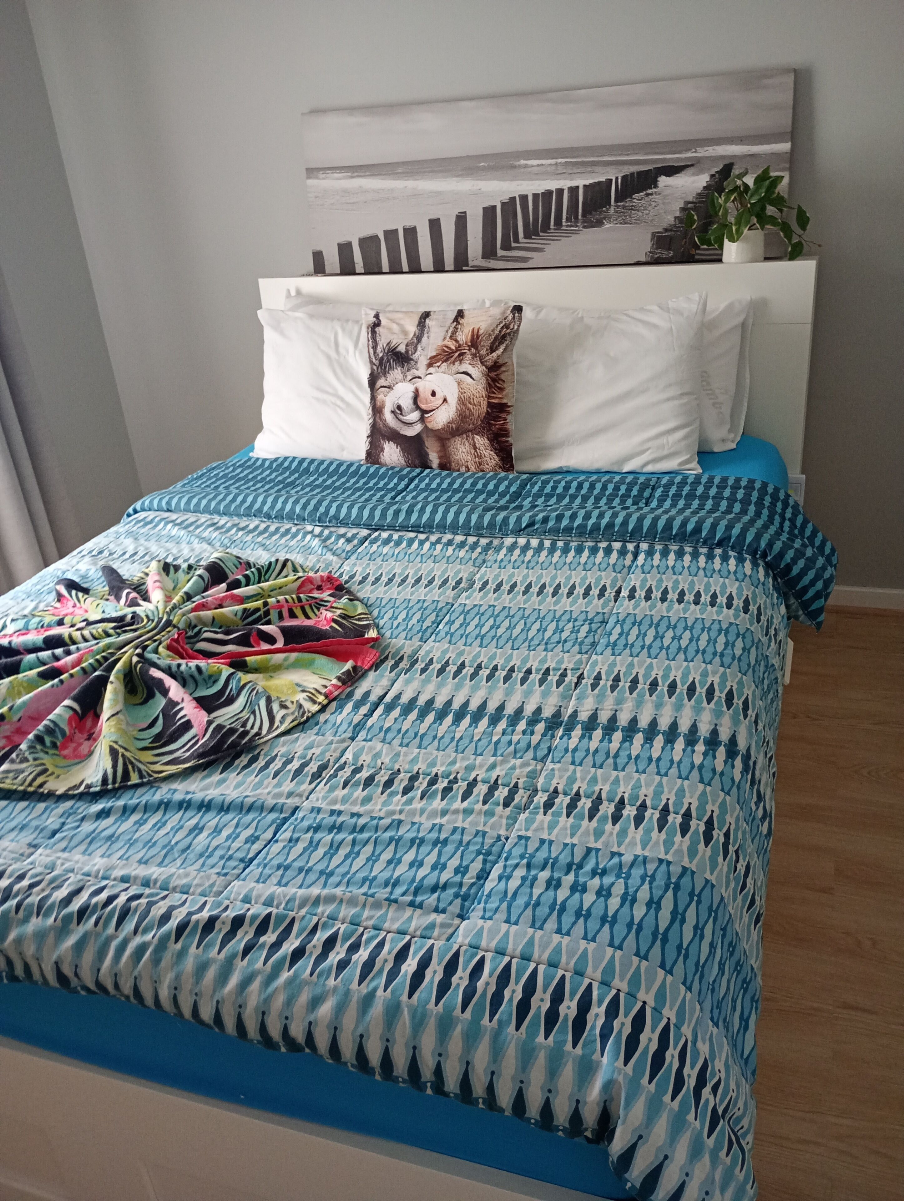 Una cama con una colcha azul estampada, un almohadón con diseño de burro y un cuadro colgado en la pared.