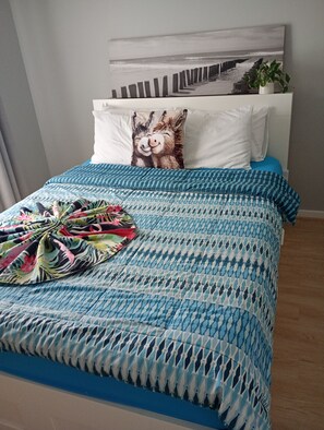 Ein Bett mit blauer, gemusterter Bettdecke, ein Kissen mit Esel-Motiv und ein Wandbild.