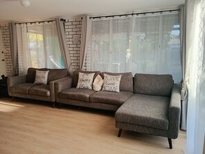 A modern living room with a sectional sofa, a brick-patterned wall, and sheer curtains. - Budget Friendly Accommodation near the Train  Station 
Cosy Private Rooms (Mandurah)