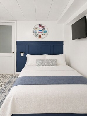 A hotel room with a bed, a round wall decoration, a television, and a door. - 1 Bedroom Apartment Near MetLife Stadium & EWR Airport (Newark)