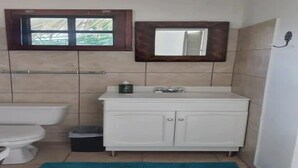 Ein Badezimmer mit Toilette, Waschbecken mit Spiegel darüber und einem Mülleimer.